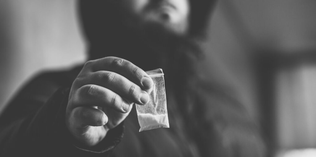 Drug dealer selling drugs junkie. Drug abuse concept and overdose concept. Mans hand holds plastic packet with cocaine powder, selective focus, black and white photo